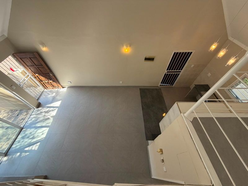 An elevated view of a spacious, empty open-plan living area featuring modern tiled floors, a staircase, and neutral wall finishes.