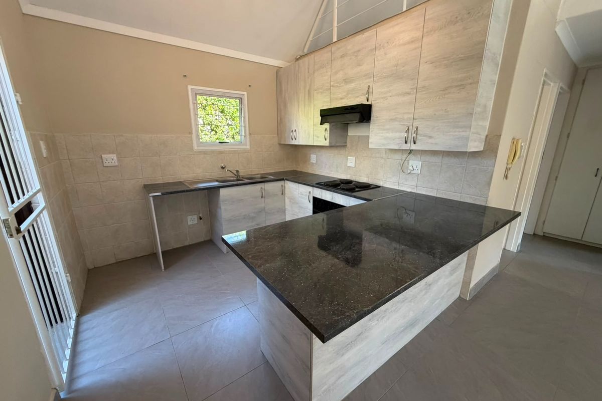 Modern kitchen featuring light wood-grain cabinetry, dark granite countertops, a built-in hob with extractor fan, and neutral tiled flooring.