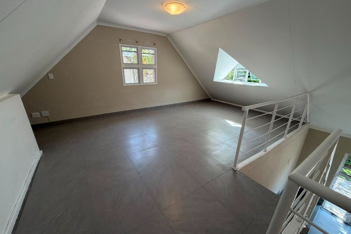 An empty loft-style bedroom featuring tiled flooring, sloped ceilings, and a metal balustrade overlooking the lower level.