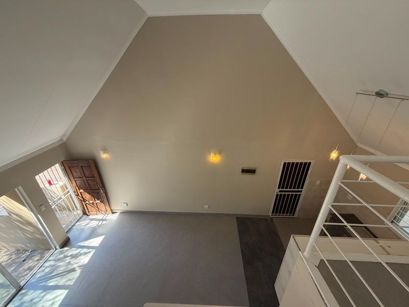 Spacious open-plan living area featuring a high vaulted ceiling, neutral tiled flooring, and direct access to the exterior through a secure timber door.