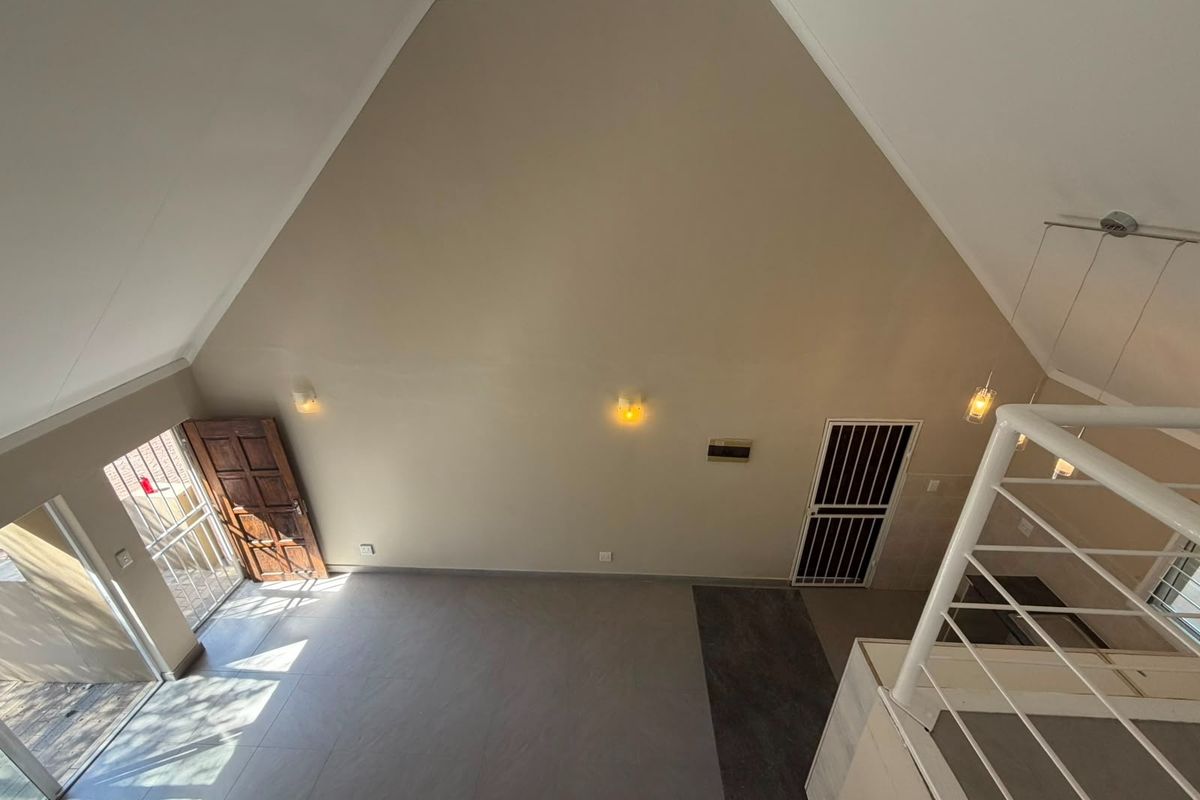 Spacious open-plan living area featuring a high vaulted ceiling, neutral tiled flooring, and direct access to the exterior through a secure timber door.