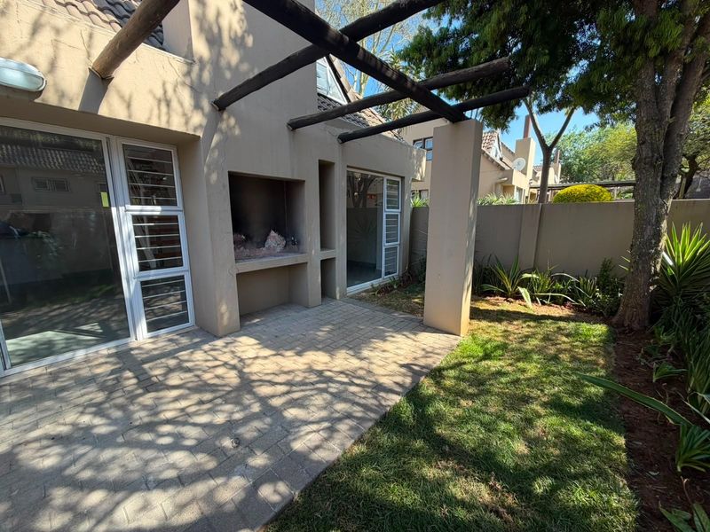 A private rear patio featuring a built-in braai, timber pergola, and paved flooring, providing direct access to the garden through sliding glass doors.