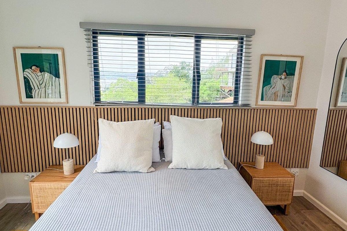 A well-maintained bedroom featuring modern timber slat wall paneling, a sloped ceiling, and large windows with venetian blinds.