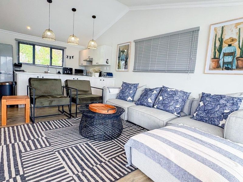 Bright open-plan living area featuring a vaulted ceiling, modern laminate flooring, and a functional kitchen space with integrated cabinetry and pendant lighting.