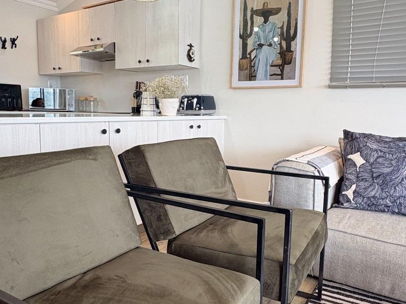 An open-plan living area featuring a compact kitchen with modern cabinetry, extractor fan, and neutral finishes, seamlessly integrated with a comfortable lounge space.