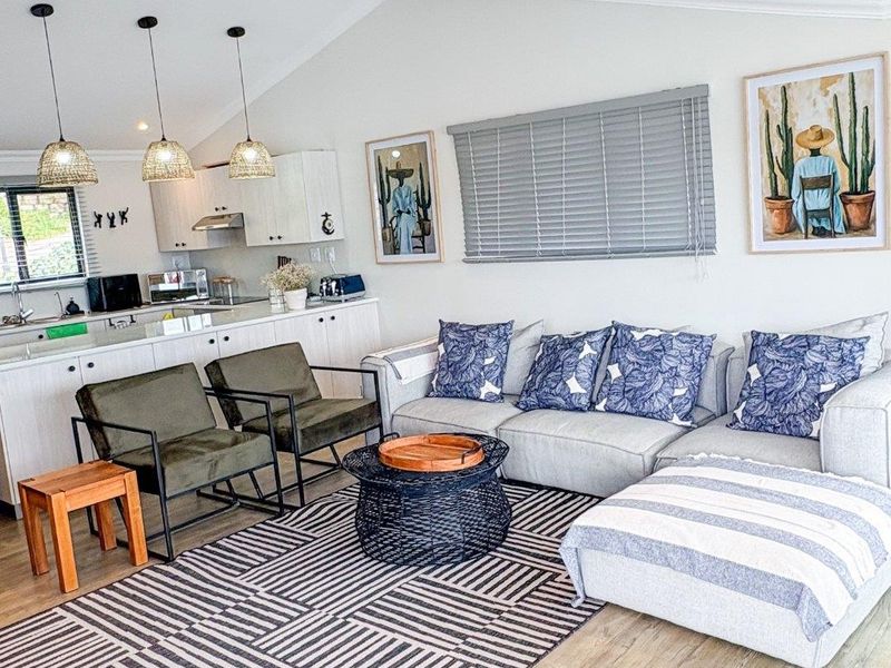 A bright open-plan living and kitchen area featuring modern cabinetry, recessed lighting, and light-toned laminate flooring.