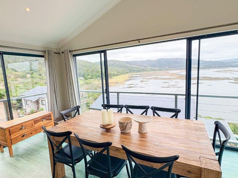 Bright dining area featuring a vaulted ceiling, recessed lighting, and expansive sliding glass doors that open to a balcony with scenic water views.
