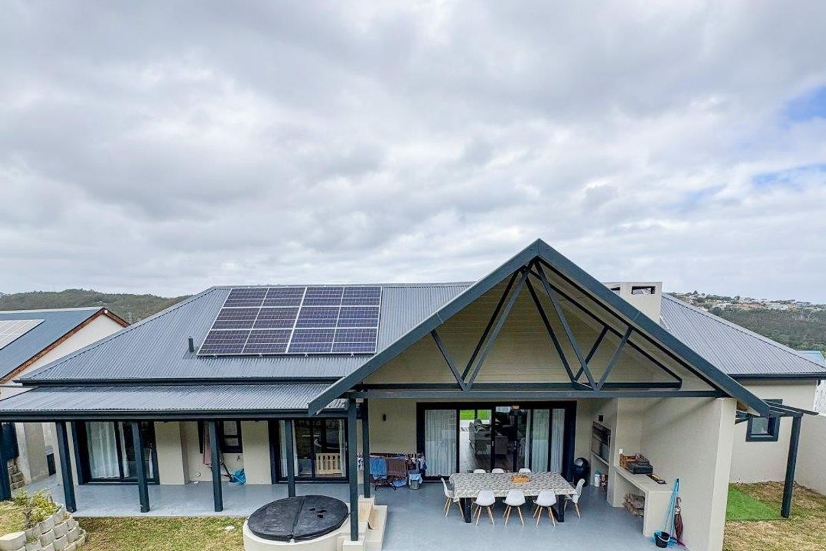 Rear view of the property featuring a spacious covered patio with built-in braai, solar panels on the roof, and direct access to the garden.