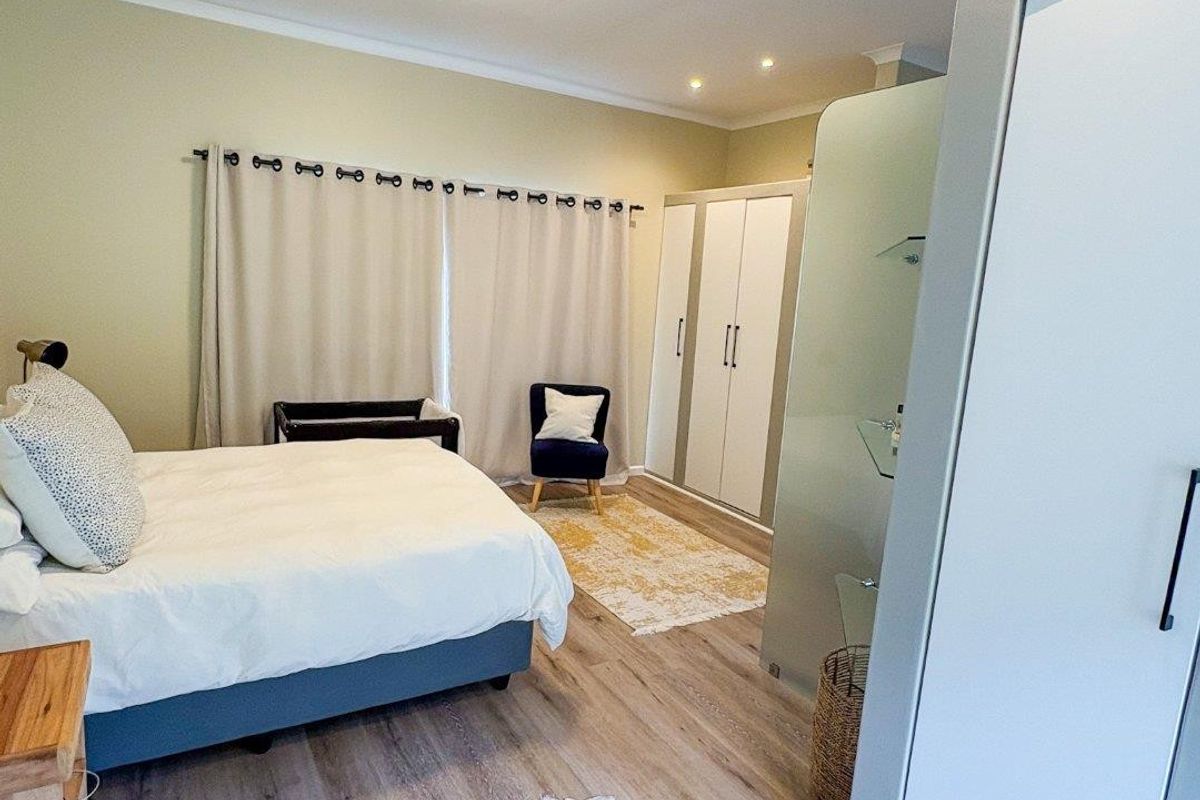 Spacious bedroom featuring modern laminate flooring, built-in cupboards, and a contemporary glass partition, creating a bright and functional living space.