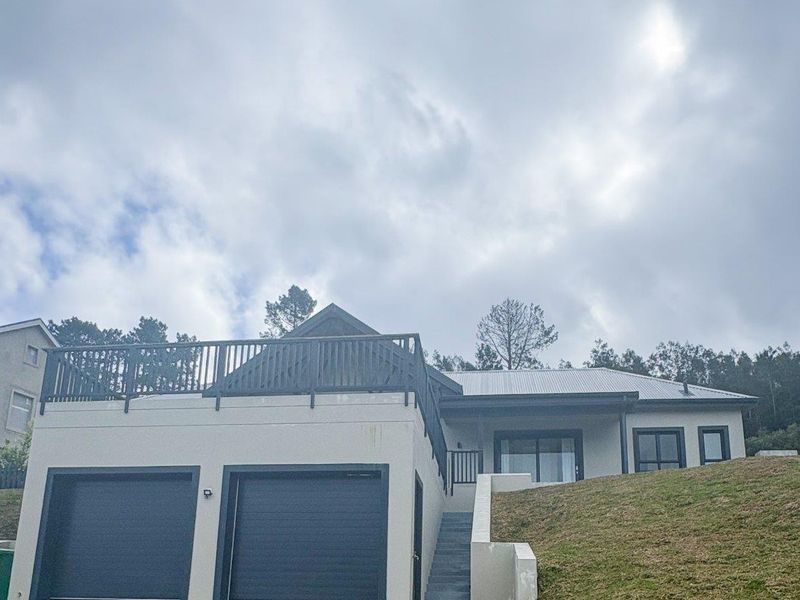 Front exterior view of a modern house featuring a double garage, a raised deck area, and a paved driveway on a sloped lot.