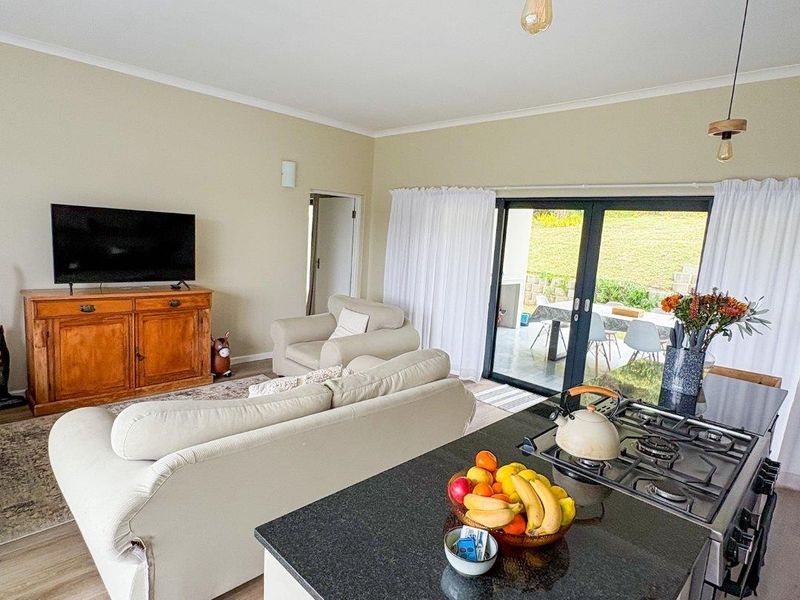 Open plan living area featuring a modern kitchen island with gas cooktop, flowing seamlessly through sliding glass doors to an outdoor patio space.