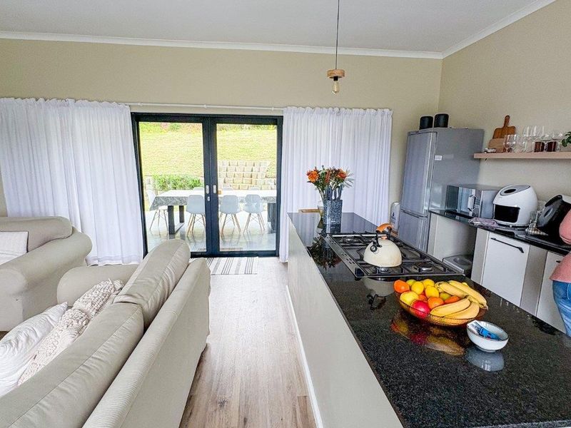 Modern open-plan living and kitchen area featuring a granite island with gas hob, laminate flooring, and sliding doors leading to the patio.
