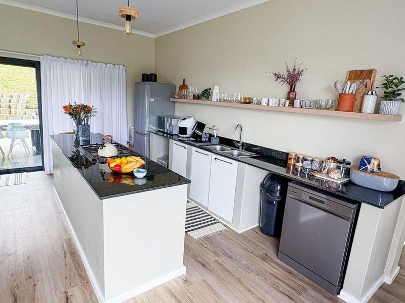 Modern kitchen featuring a central island with a gas hob, granite countertops, integrated dishwasher, and sleek cabinetry with open shelving.