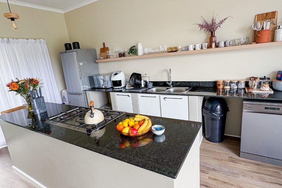 Modern kitchen featuring a central island with a granite countertop, gas hob, double sink, and open shelving for storage.