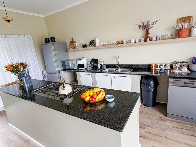 Modern kitchen featuring a central island with a granite countertop, gas hob, double sink, and open shelving for storage.