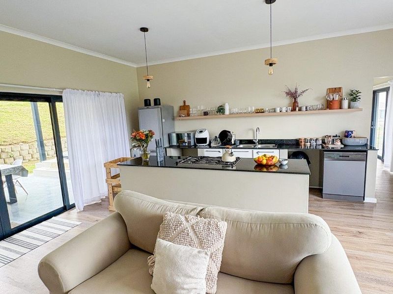 Modern open-plan living area featuring a well-appointed kitchen with granite countertops, gas hob, and seamless flow to the outdoor patio through sliding glass doors.