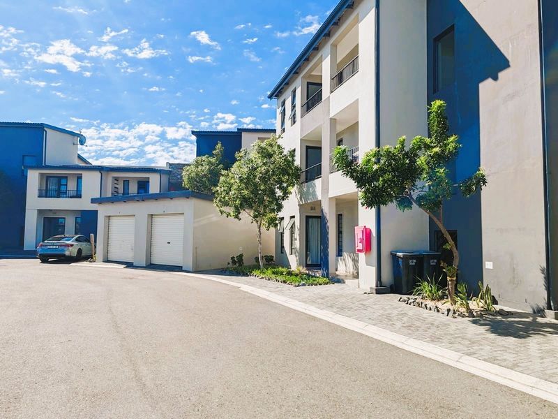 Exterior view of a modern apartment complex featuring paved driveway access, integrated garages, and multi-level balconies under a clear blue sky.