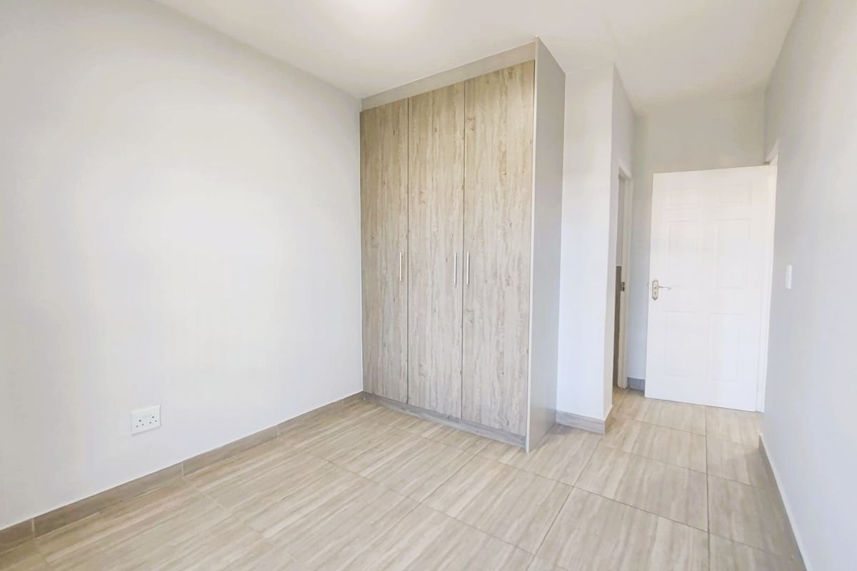 A bright, empty bedroom featuring modern wood-look tiled flooring and a built-in wardrobe with light wood-grain finish.