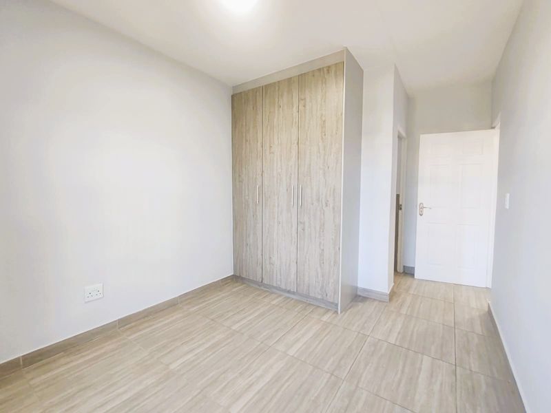 A bright, empty bedroom featuring modern wood-look tiled flooring and a built-in wardrobe with light wood-grain finish.