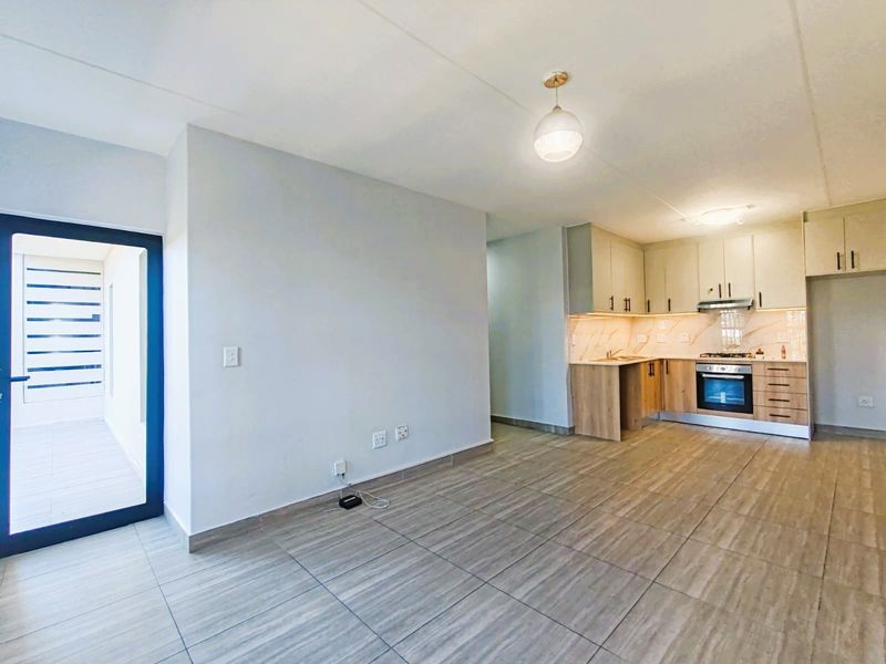 An open-plan living and kitchen area featuring modern cabinetry, built-in appliances, tiled flooring, and direct access to an outdoor balcony.