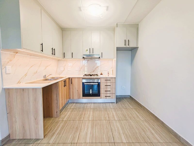 Modern kitchen featuring light wood-tone lower cabinets, white upper cabinetry, marble-look splashback, built-in oven, gas hob, and tiled flooring.