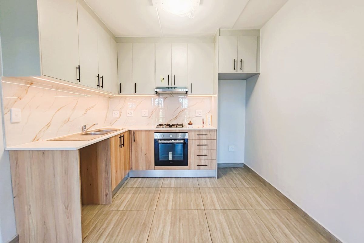 Modern kitchen featuring light wood-tone lower cabinets, white upper cabinetry, marble-look splashback, built-in oven, gas hob, and tiled flooring.