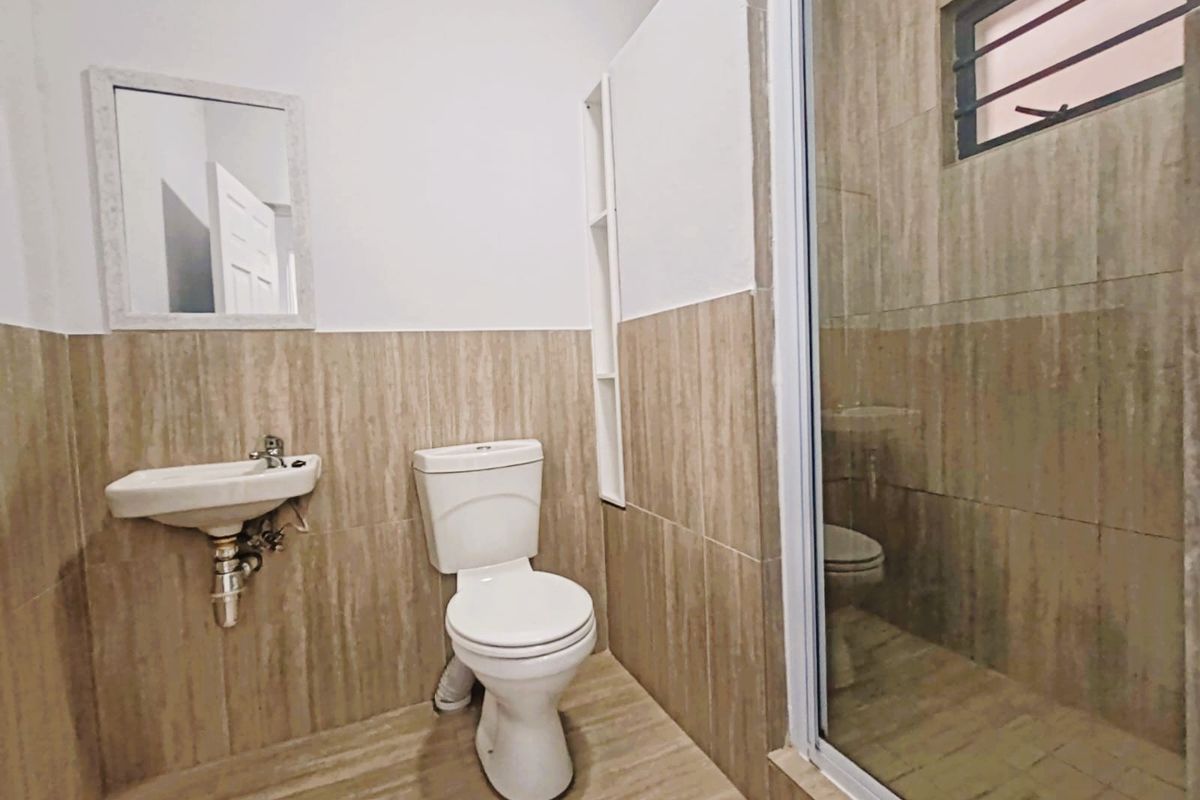 A functional bathroom featuring a wall-mounted basin, toilet, and a tiled shower enclosure with neutral wall and floor tiling.