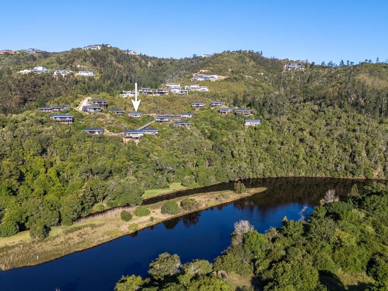 Aerial view of a hillside residential estate nestled in a lush, forested landscape overlooking a river.