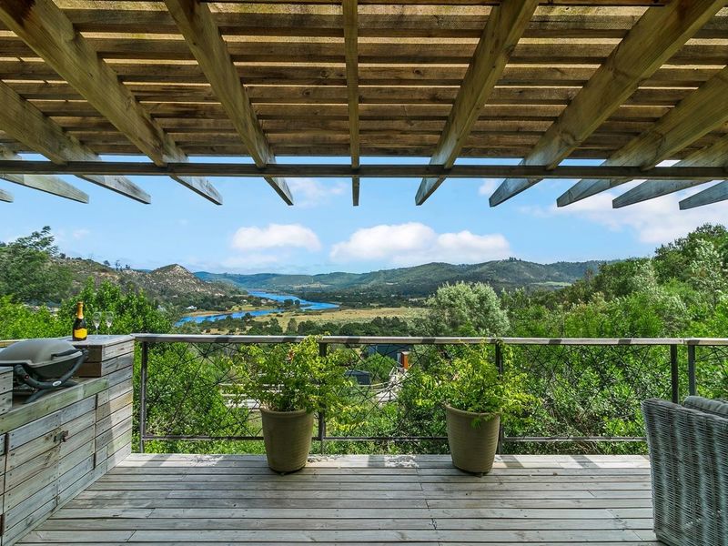 Covered timber deck featuring a pergola, built-in cabinetry, and metal balustrade, offering expansive views of the surrounding valley and river.