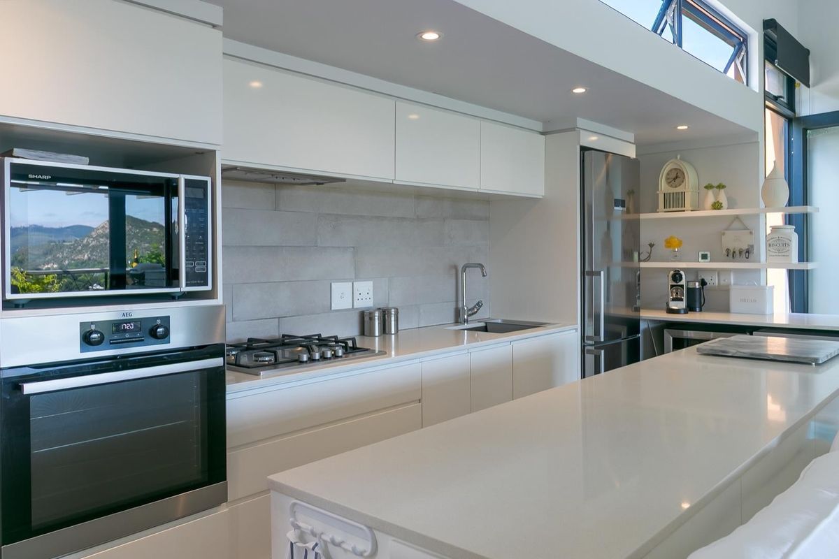 Modern kitchen featuring sleek white cabinetry, stone countertops, a central island, built-in appliances, and a stylish tiled backsplash.