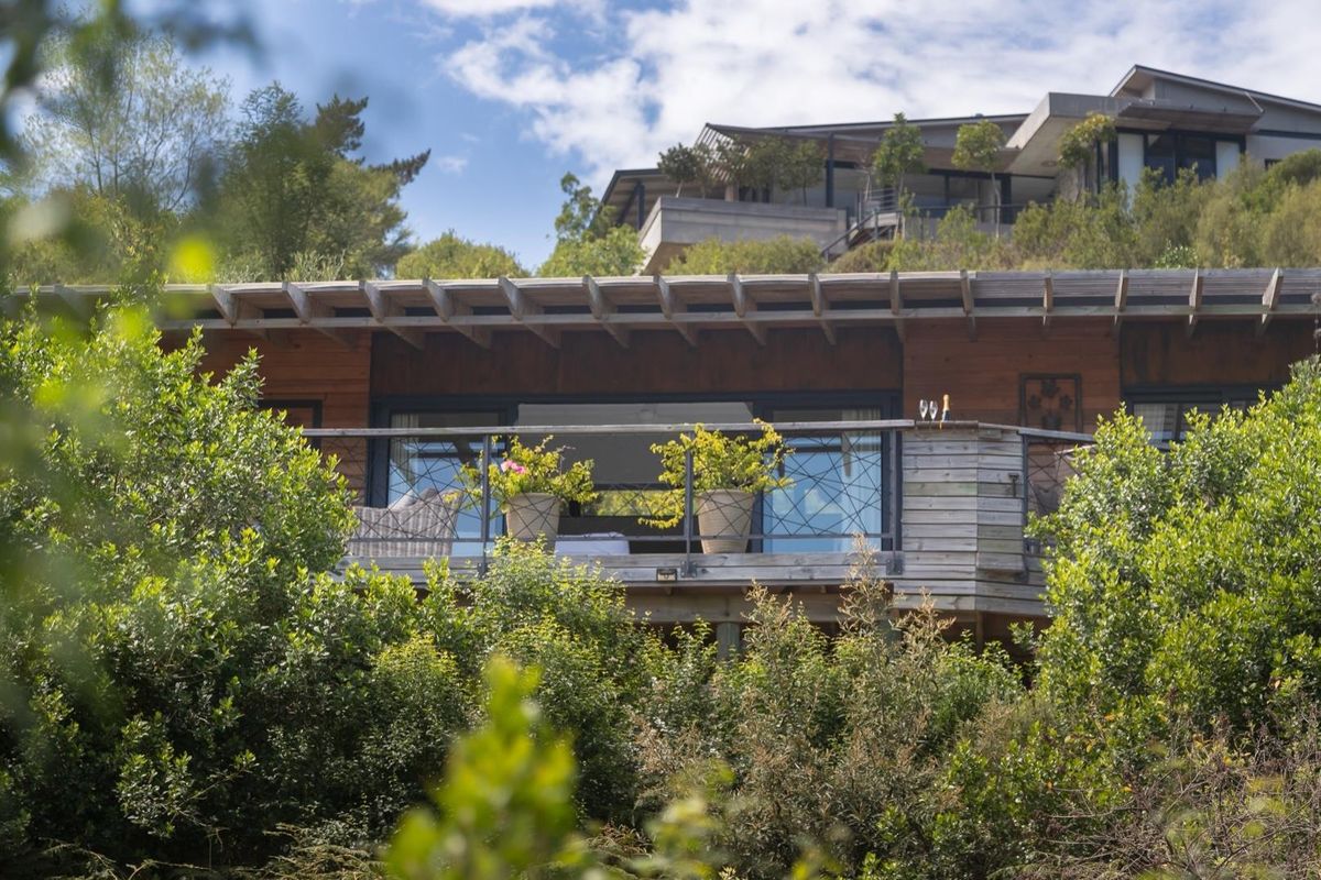 A rear view of the property featuring timber cladding, a wooden pergola, and a balcony with a metal balustrade overlooking lush greenery.