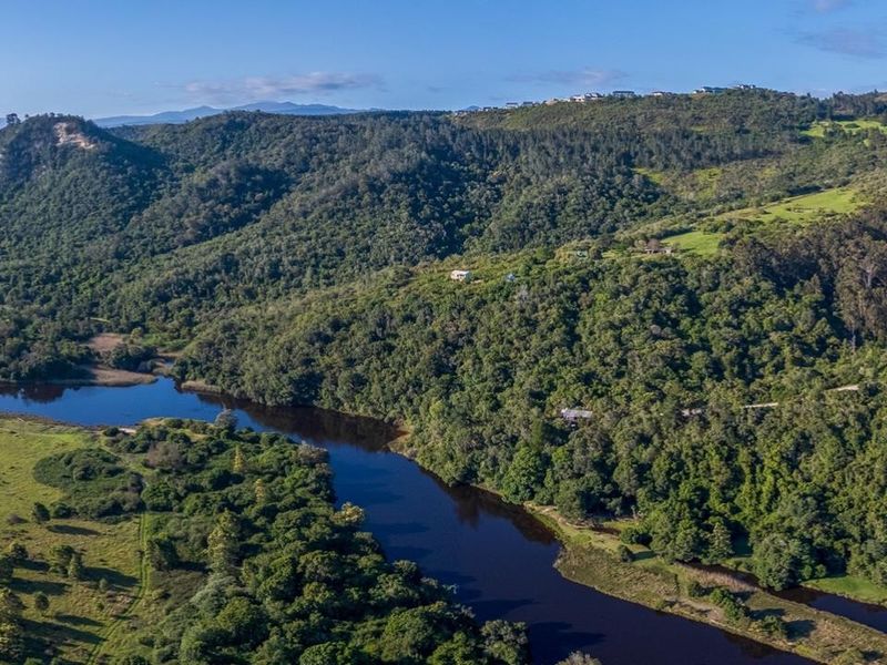 An aerial view of a scenic landscape featuring a winding river, lush green hills, and a residential development nestled on the hillside.