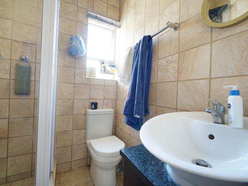 A compact bathroom featuring a shower enclosure, toilet, and vanity basin with tiled wall finishes.