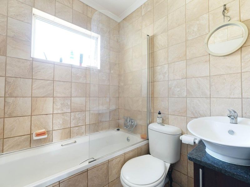 A functional bathroom featuring a bathtub with a glass screen, a vessel sink on a stone vanity, and neutral wall tiling.
