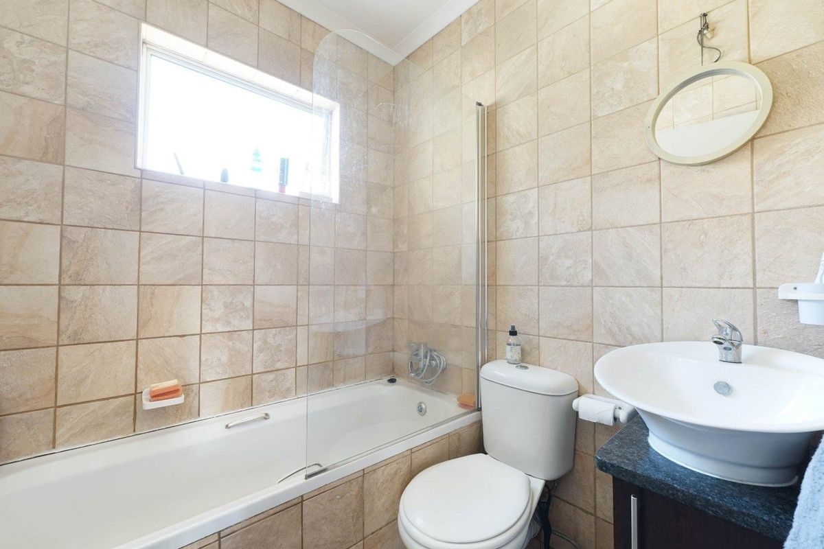 A functional bathroom featuring a bathtub with a glass screen, a vessel sink on a stone vanity, and neutral wall tiling.