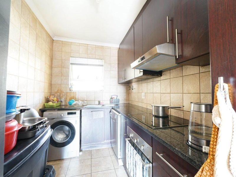 Compact kitchen featuring dark wood cabinetry, granite countertops, ceramic tiling, and built-in appliances including an oven, hob, and washing machine.