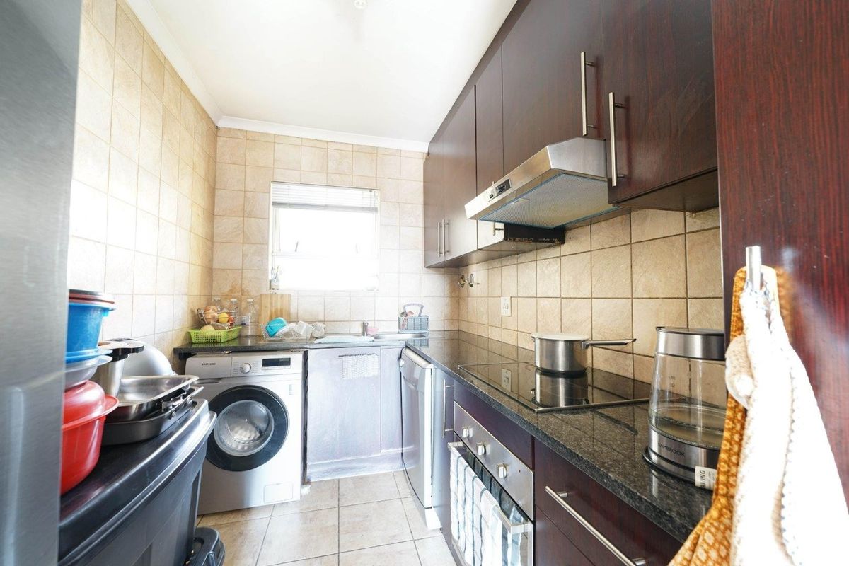 Compact kitchen featuring dark wood cabinetry, granite countertops, ceramic tiling, and built-in appliances including an oven, hob, and washing machine.