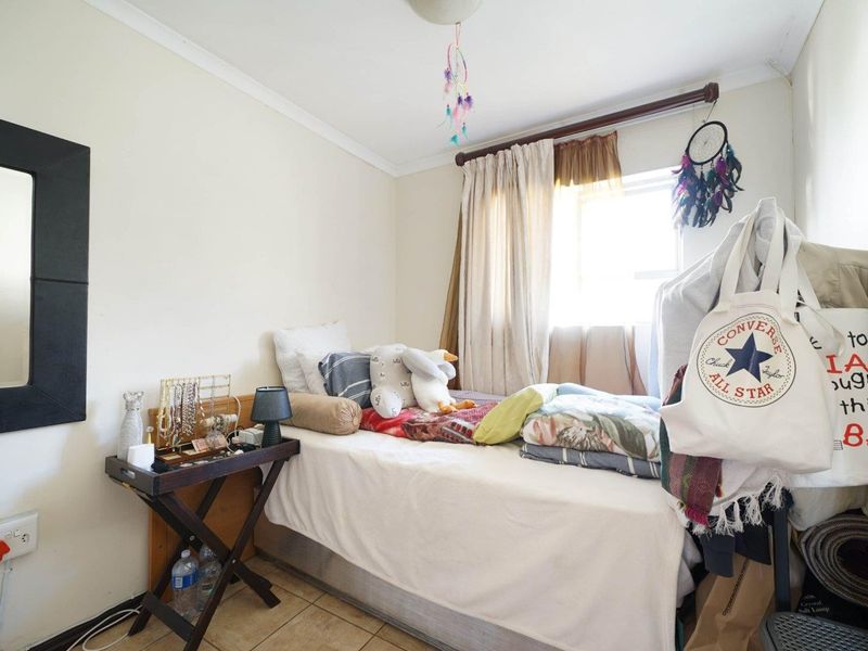 A compact bedroom featuring tiled flooring, a window with curtain rod, and standard electrical fixtures.