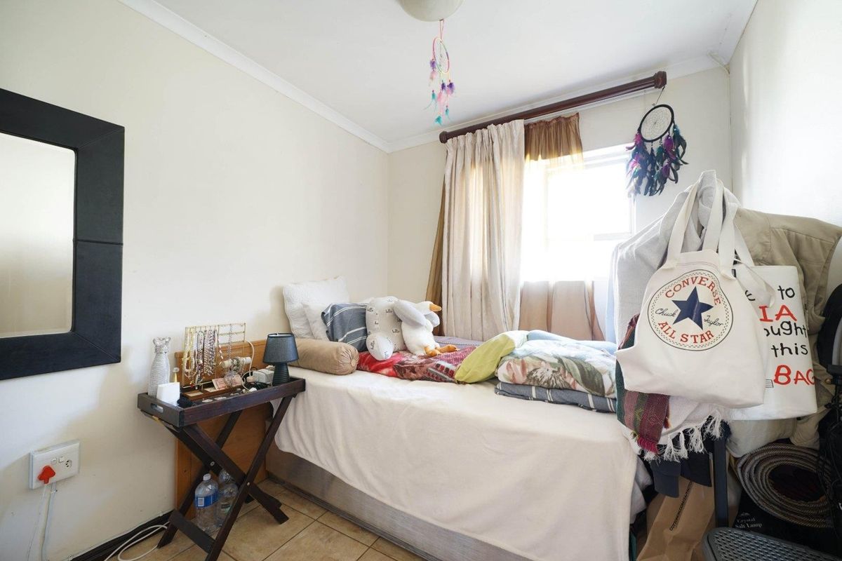 A compact bedroom featuring tiled flooring, a window with curtain rod, and standard electrical fixtures.