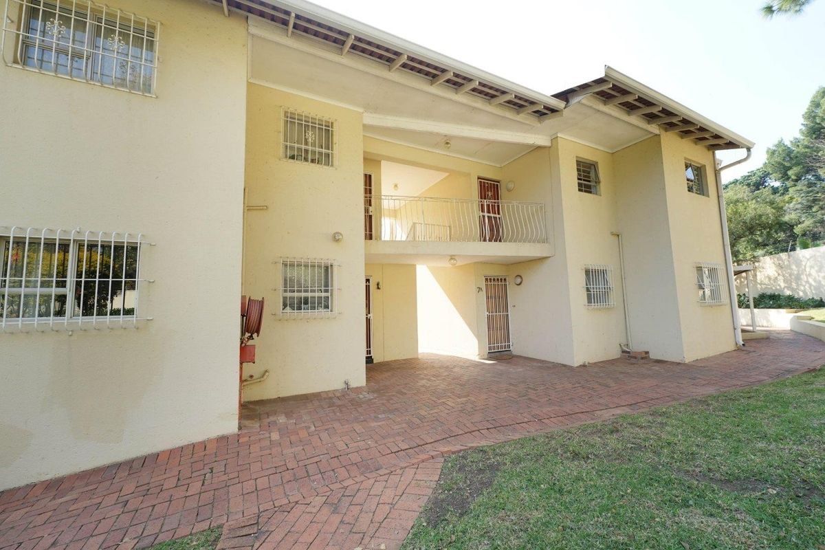 Rear view of the apartment building featuring brick paving, a balcony, and security bars on windows.