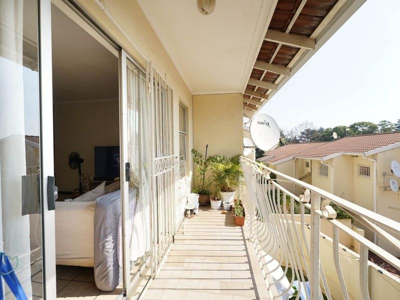 A covered balcony featuring tiled flooring, a metal security gate, and a metal balustrade, providing an outdoor extension to the living area.