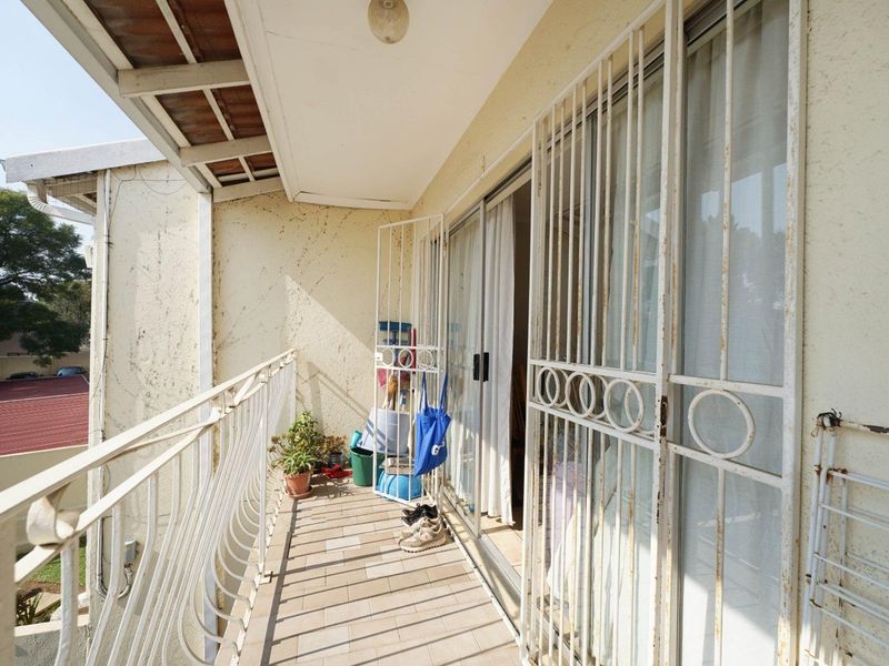 A balcony featuring tiled flooring, a metal security gate, and a balustrade, showing signs of wear on the exterior walls and metal fixtures.