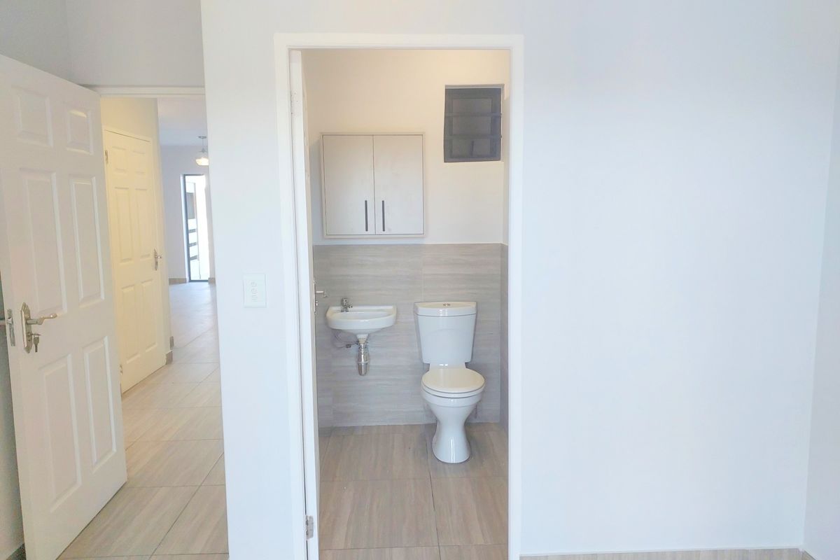 A clean, compact bathroom featuring a wall-mounted basin, toilet, and overhead storage cabinet with neutral tiled finishes.