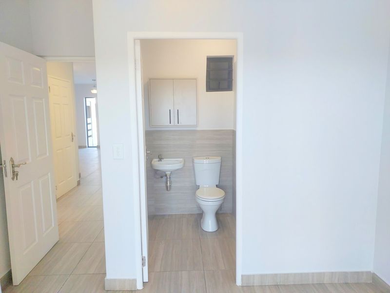 A clean, compact bathroom featuring a wall-mounted basin, toilet, and overhead storage cabinet with neutral tiled finishes.