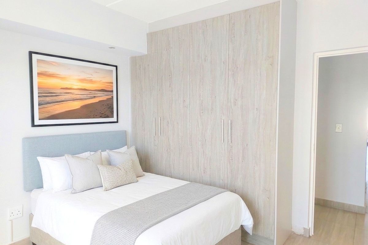 A well-maintained bedroom featuring light wood-finish built-in cupboards, neutral laminate flooring, and clean, modern finishes.