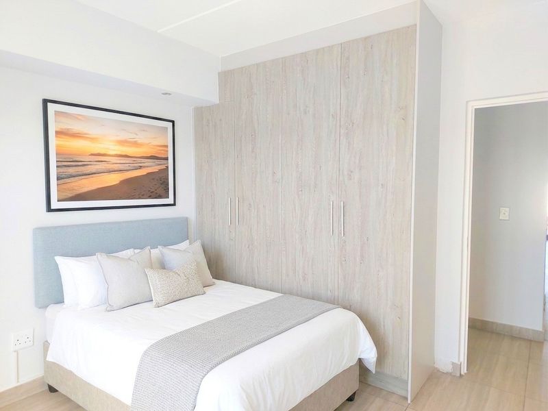 A well-maintained bedroom featuring light wood-finish built-in cupboards, neutral laminate flooring, and clean, modern finishes.