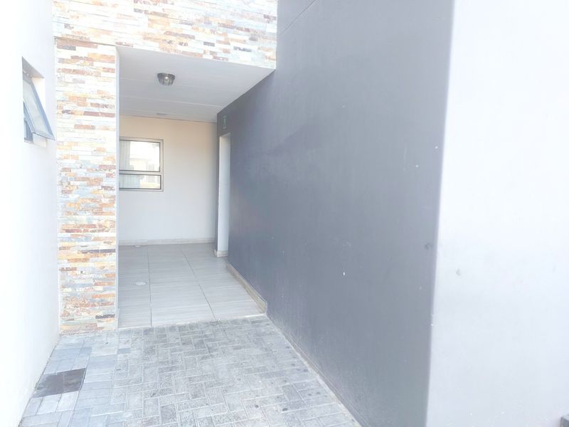 A clean, modern apartment entrance featuring stone cladding, paved driveway, and tiled flooring leading to the main doorway.