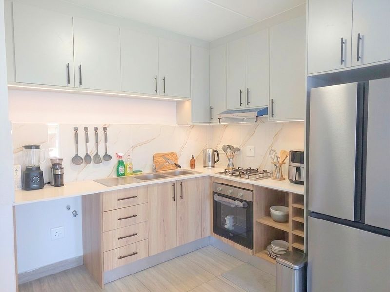 Modern kitchen featuring light wood cabinetry, stone countertops, marble-look splashback, integrated gas hob, oven, and extractor fan with under-cabinet lighting.