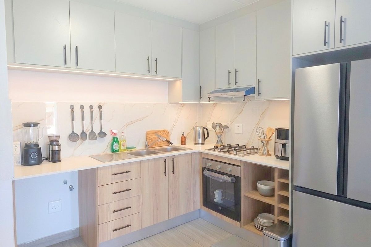 Modern kitchen featuring light wood cabinetry, stone countertops, marble-look splashback, integrated gas hob, oven, and extractor fan with under-cabinet lighting.