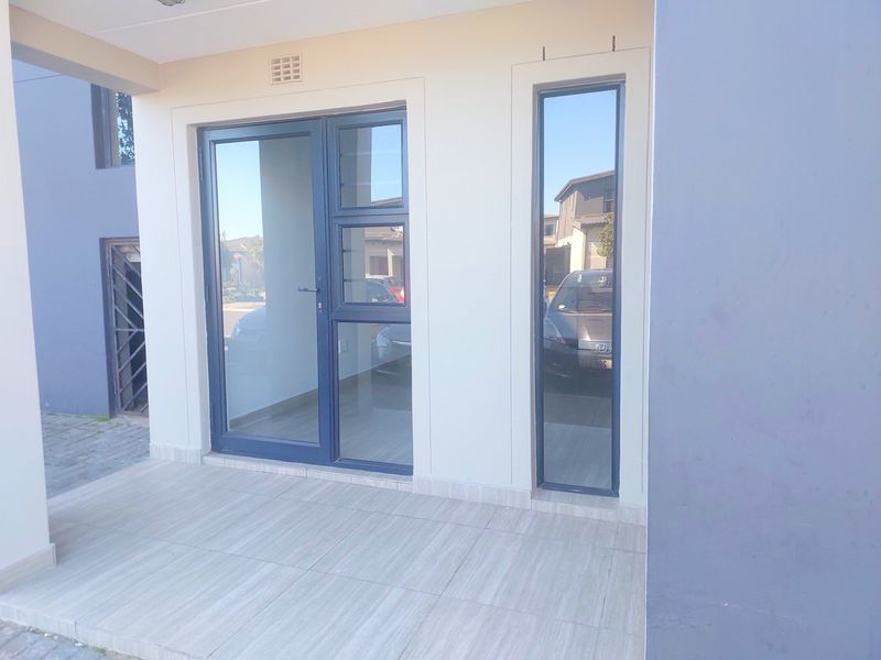 A clean, modern entrance area featuring tiled flooring and a contemporary aluminium-framed glass door with a matching fixed sidelight.
